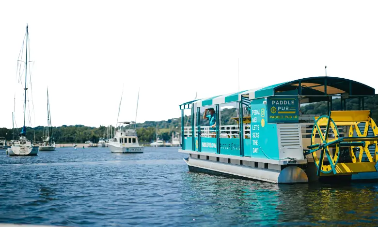 A Paddle Pub boat moored among yachts in a marina