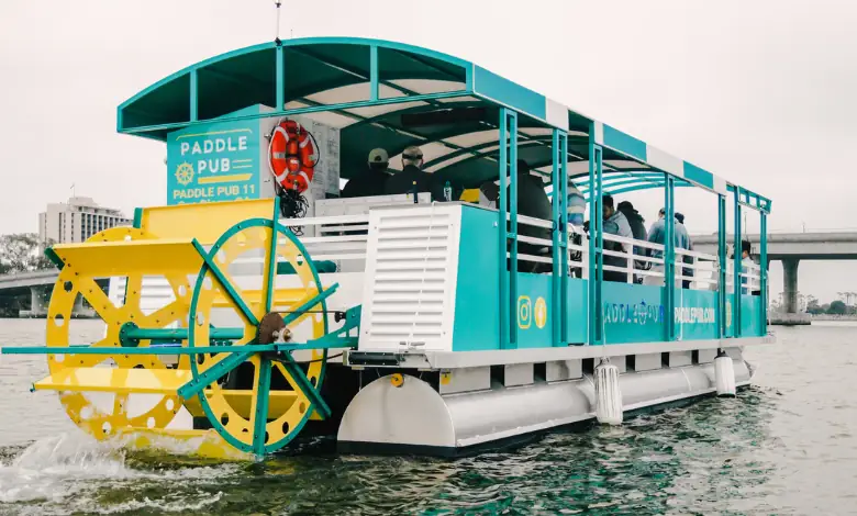A Paddle Pub boat with its yellow paddle wheel on the water