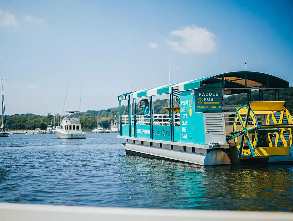 A Paddle Pub boat cruising past moored yachts in a marina