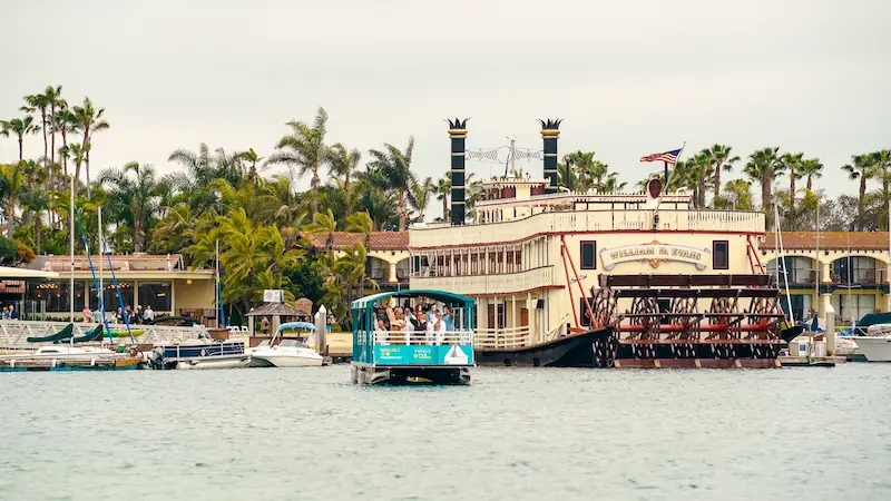 A Paddle Pub boat alongside a paddle steamer on a palm-lined waterfront